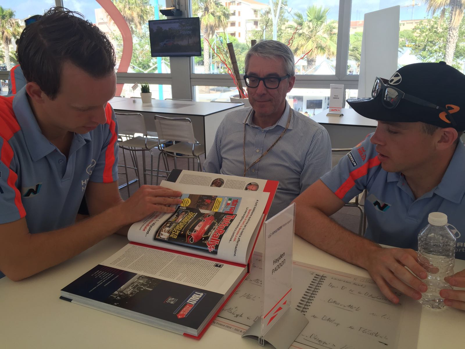 Leo Todisco Grande mostra il libro a Hayden Paddon e Kevin Abbring piloti ufficiali Team Hyundai WRC