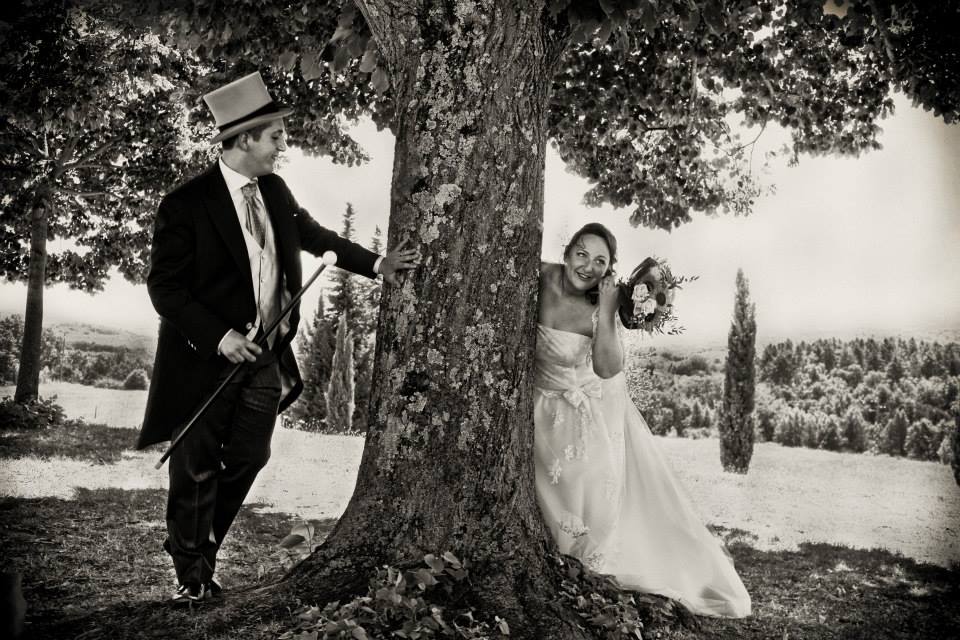 sposi all'ombra di un grande albero, scherzosi tra loro, con bouquet, cappello e cilindro, Toscana