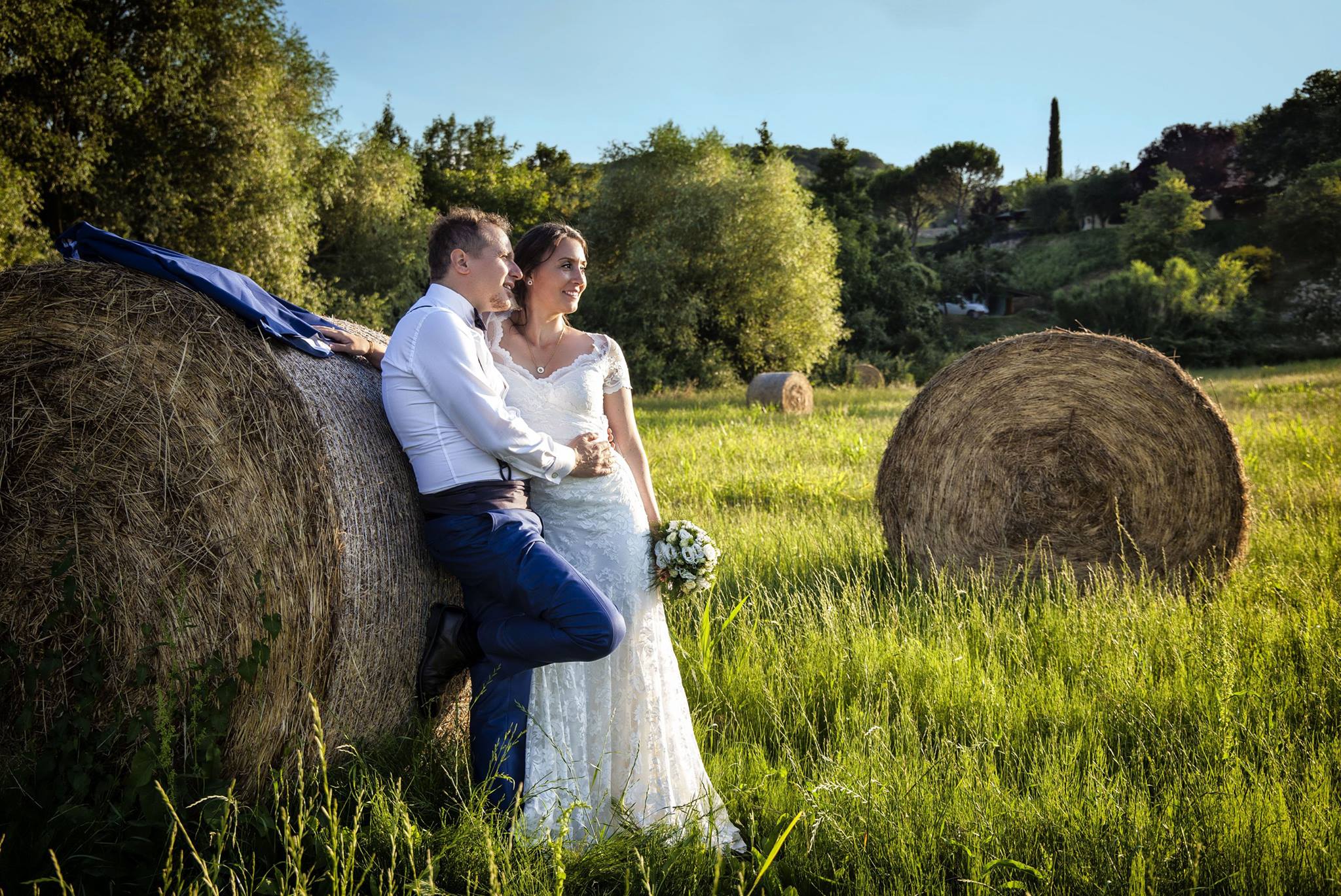 sposi in un campo di grano appoggiati a una balla di fieno baciati dalla luce del sole